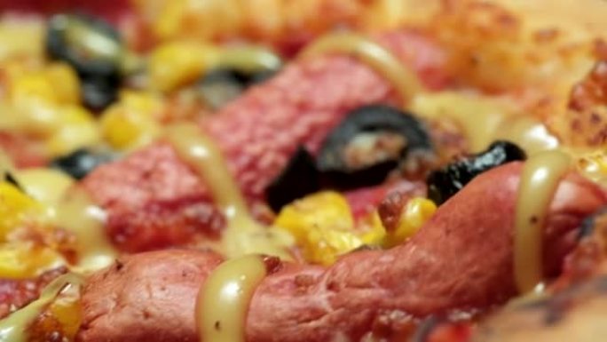 特写旋转的热披萨的镜头，里面有香肠、橄榄、奶酪和芥末和蜂蜜。