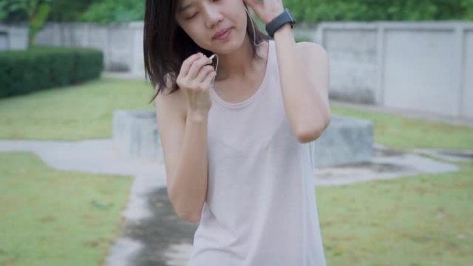 美丽的亚洲女子戴着耳塞，使用智能手表，在去公园跑步前伸展身体