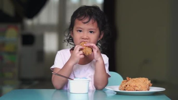 可爱的东南亚小女孩穿着白色上衣在家吃油炸脆皮鸡肉的特写