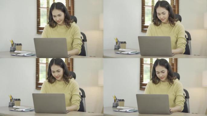 在笔记本电脑上工作的亚洲女性看着笔记本电脑屏幕，通过互联网通信系统在家放松工作