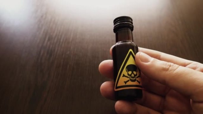 手拿着一小瓶毒药，上面有一个黄色的有毒标志，代表一个头骨和两个骨头图标-危险的混合物