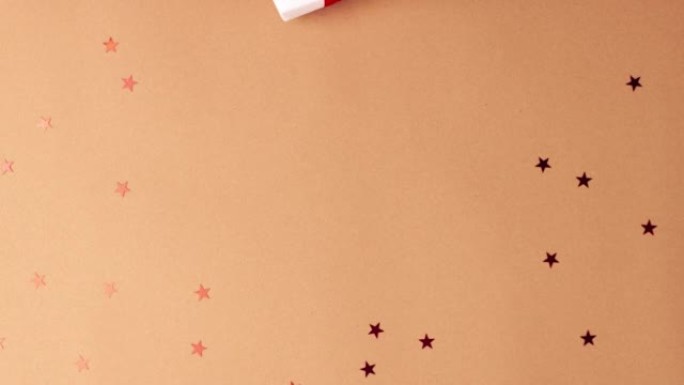 穿着白色毛衣的人的手拿走了一份白纸礼物，上面有一个红色缎带蝴蝶结，棕色背景是红色星星。定格动画圣诞假
