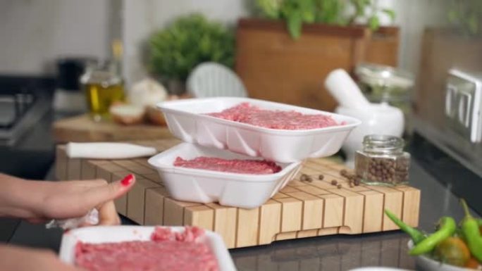 时髦的红色修指甲的女人打开带有牛肉末的白色塑料容器，在厨房工作场所准备制作多汁的家庭汉堡。专业木板上