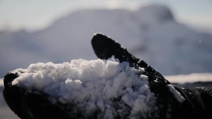 冬季手套中人的手的特写在模糊的背景上高海拔上夹着许多新鲜的雪