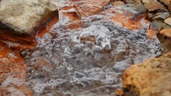 带有矿物质气体和健康盐气泡的地下纯净水冒泡的慢动作视频。矿泉水间歇泉周围的红色石头。对肠道有益