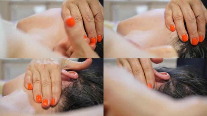 特写按摩女性颈部和枕部区域在按摩面部和头部的过程中，用美容师按摩师的手与红色修指甲。面部和头皮护理