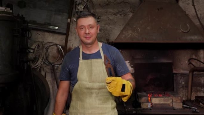 一个铁匠的肖像，用锤子和大钳子在一个旧的锻炉中。