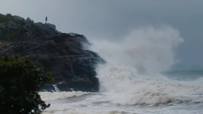人站在岩石上，看着巨浪在海洋风暴中冲破岩石