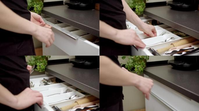 穿着黑色t恤和短裤的女孩或女人走到餐具抽屉，拿起两个闪亮的铬叉。早上早餐或午餐或晚餐的概念。吃和使用