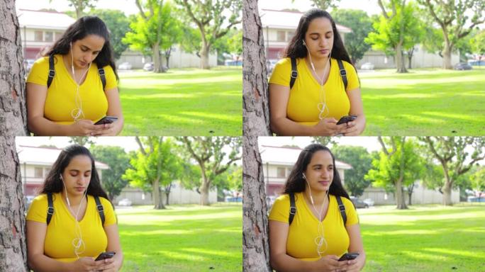 一个带耳塞和智能手机的西班牙裔女孩在公园听音乐和发短信的高清视频