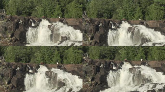 人们坐在瀑布顶上的美丽镜头和背景中的绿树