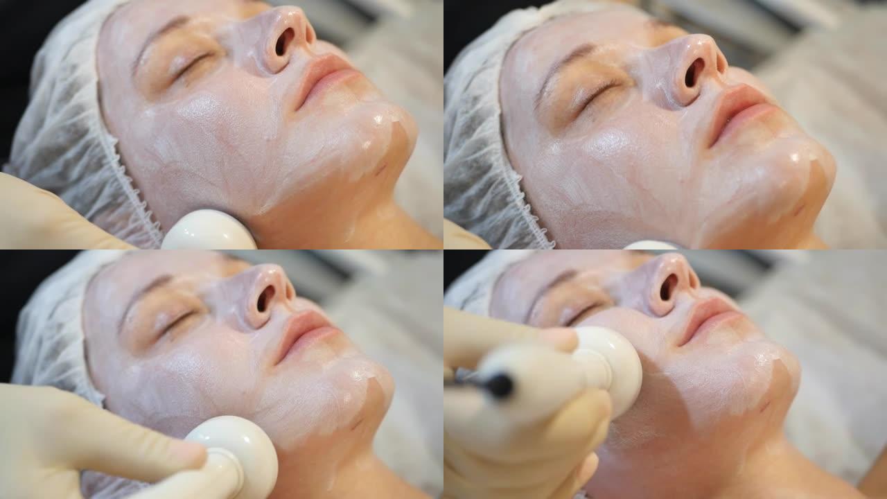 详细信息: 应用金色胶囊的乳霜，在美丽的年轻女子的脸上进行超声波电泳程序的过程。化妆品业务