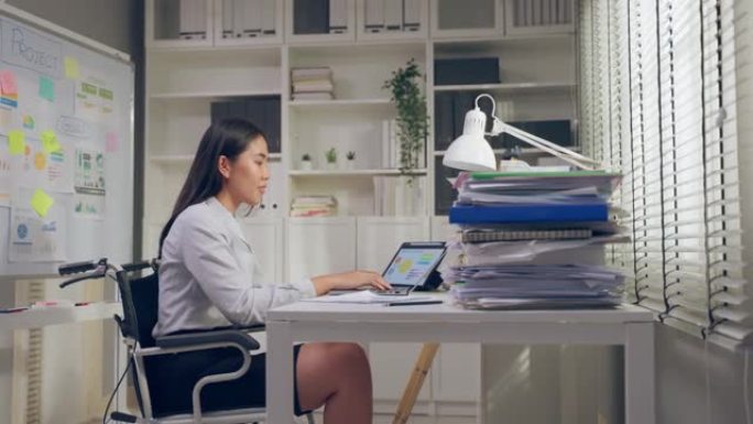 亚洲年轻的腿部截肢者女商人在办公室工作时幸福快乐。穿着正式服装的有吸引力的无腿员工坐在桌子上，并在公