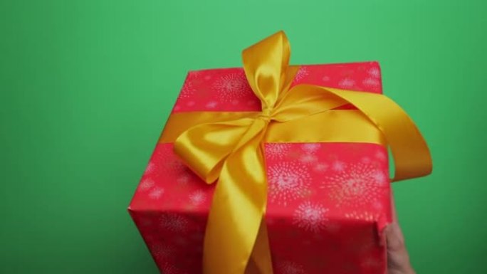 特写女人的手握着一个红色的礼品盒在她的手掌中颤抖，并在绿色屏幕色度键的背景下降低。赠送礼物或惊喜。庆