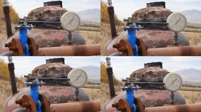 一个过时的泵站的特写镜头，用于从地下抽水，用农作物灌溉田地。生锈的井由水箱，阀门和水压表组成。