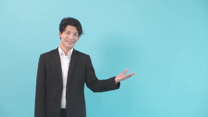 年轻的亚洲男子穿着西装，商人，手掌在孤立的蓝色背景上翻拍广告，在工作室拍摄肖像