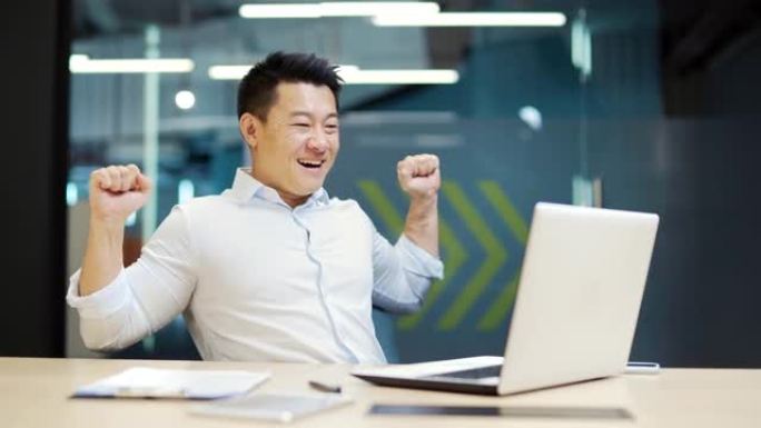 对结果满意的员工成功完成项目或工作。快乐快乐的亚洲上班族商人坐在工作场所的办公室里，在笔记本电脑上工
