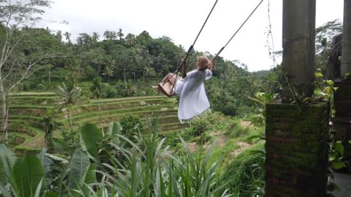 巴厘岛稻田。一名中年妇女坐在老式的木制秋千上。它像钟摆一样来回摆动。当挥杆达到极点时，女人屏住呼吸。