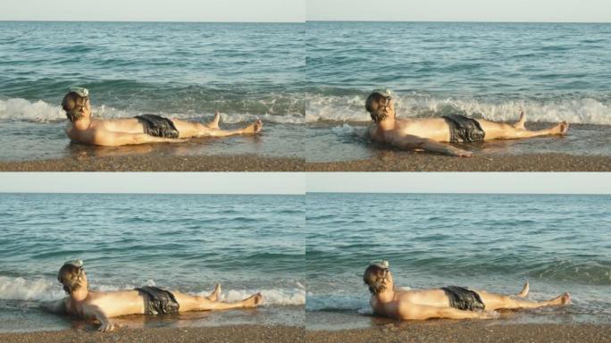 一个戴着水肺潜水面具的人躺在海边，双手张开，被海浪覆盖。