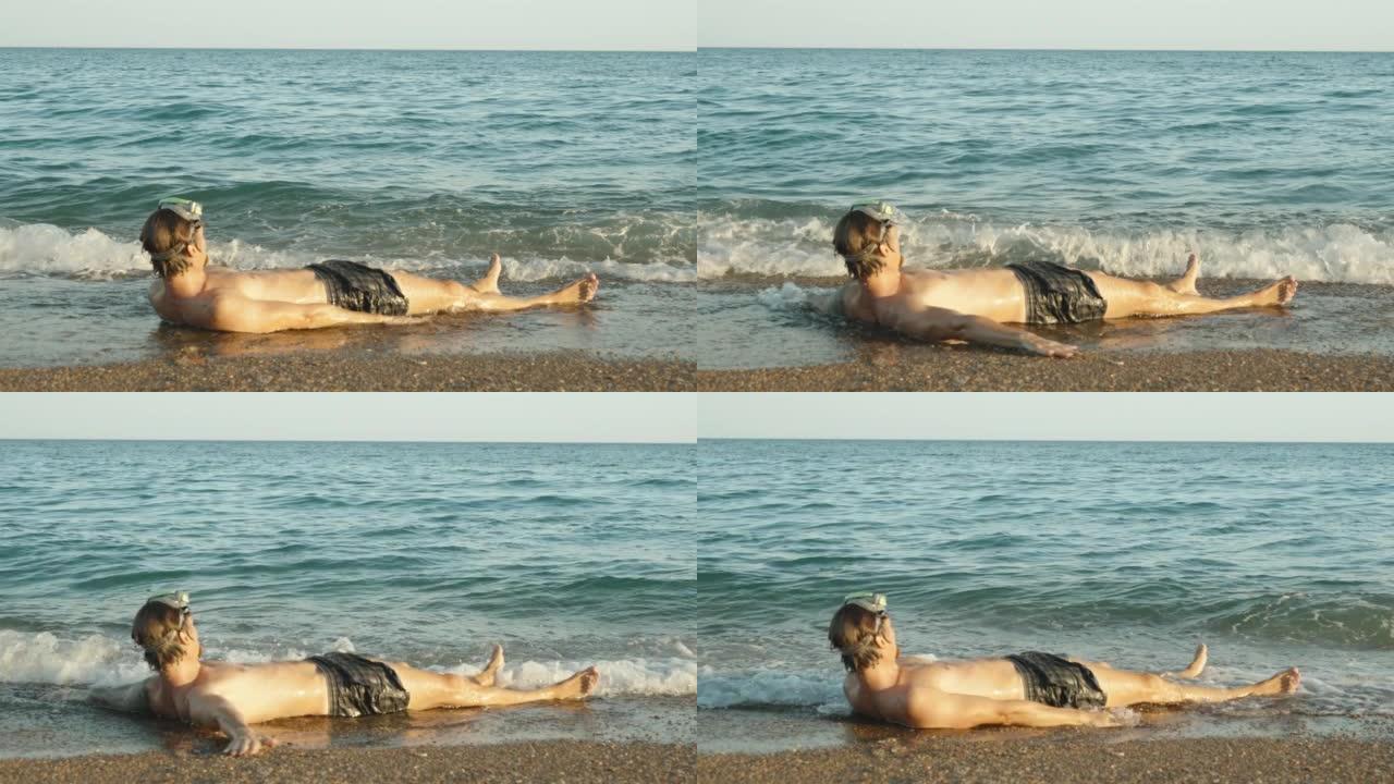 一个戴着水肺潜水面具的人躺在海边，双手张开，被海浪覆盖。