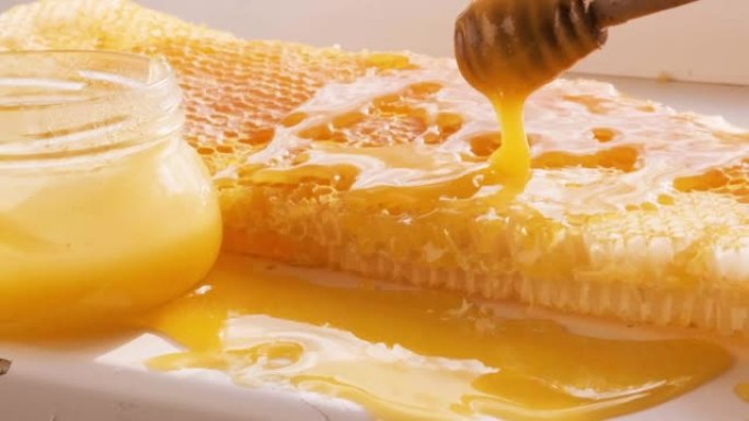 蜂蜜从蜂窝状框架上的蜜勺上滴下来。天然液体蜂蜜从滴头流到蜂蜡碎片上。