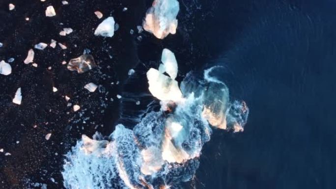 带有光反射的纯净蓝色海水波浪在冰岛的火山海滩上粉碎了冰山