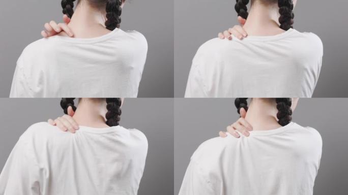 关节炎和软骨病。小辫子的女人用手握住肩膀，感到疼痛。后视图，特写。灰色背景。韧带和关节损伤的概念
