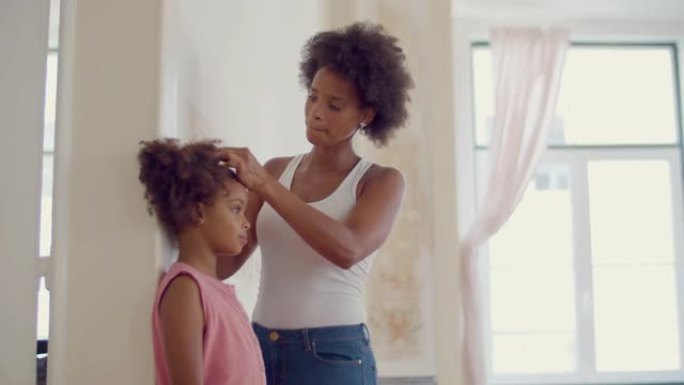 年轻的黑人妇女在墙上测量女儿的身高。