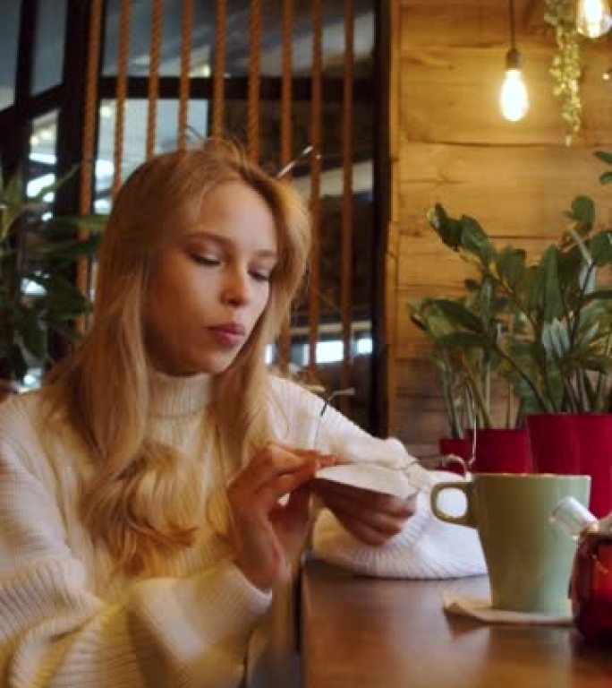 年轻女子坐在咖啡馆擦眼镜表面。垂直4k镜头。