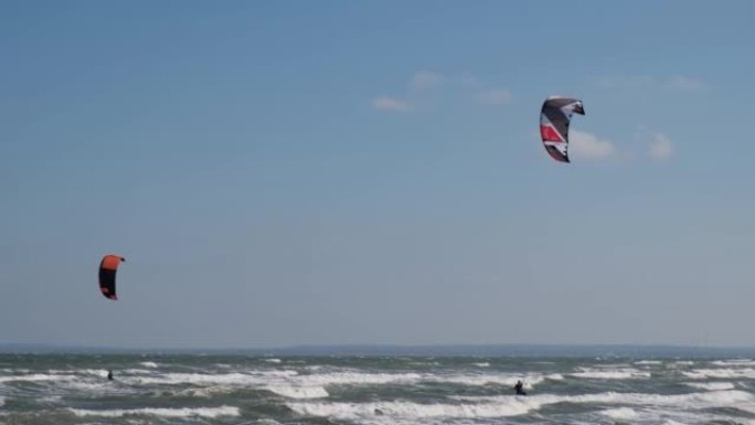 一个穿着潜水服的人穿着降落伞在海浪中滑行。一个年轻人在空中对着天空表演魔术。水上运动，风筝冲浪，滑翔