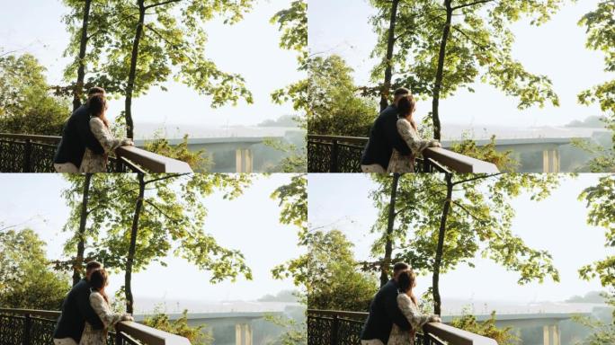 侧视图年轻可爱的夫妇在秋天公园的栏杆附近紧密地呆在一起，拥抱，享受愉快的聊天。
