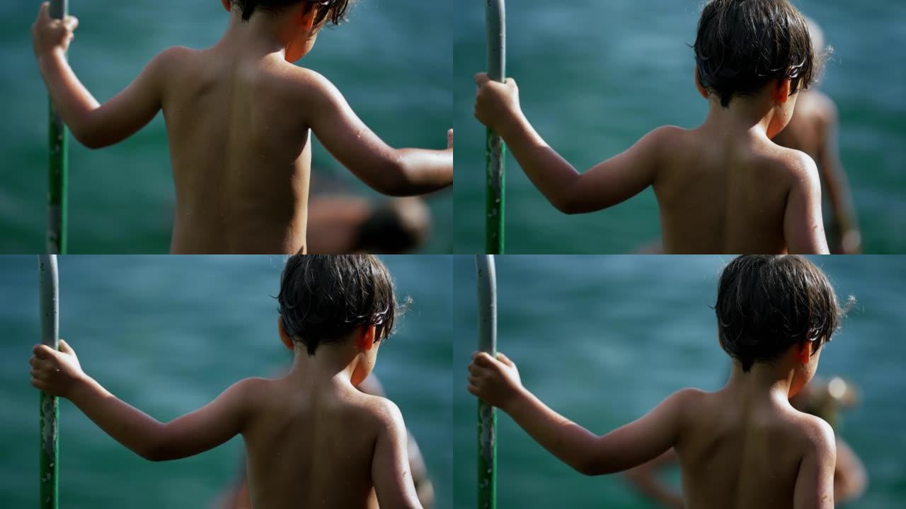 为了安全起见，湿小男孩沿着湖边爬下台阶，抓住金属棒。一个享受暑假的孩子