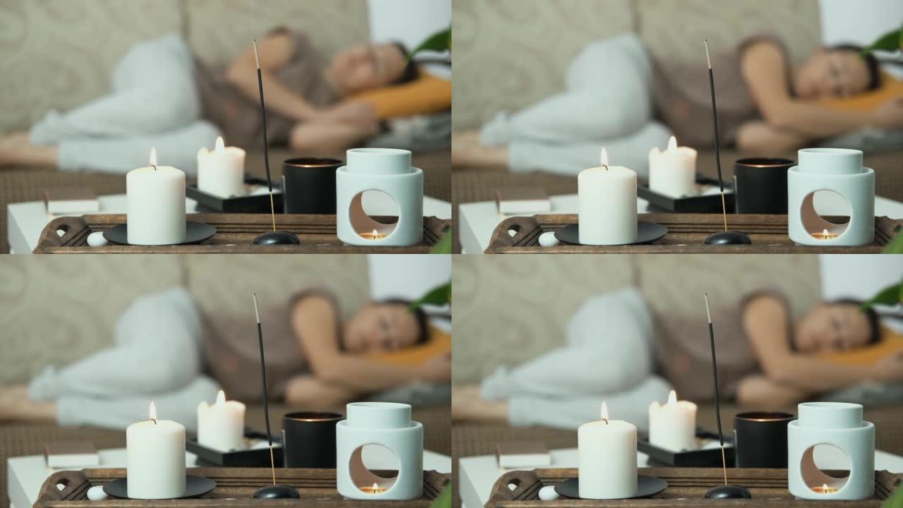 关闭香薰蜡烛和香薰灯。在背景中，女人躺在沙发上睡觉，放松。抗压力和整体休息。心理健康概念。