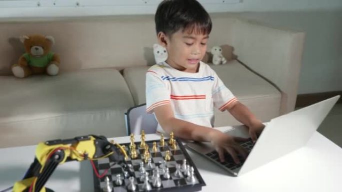 亚洲小男孩在笔记本电脑上为机器手臂编程下棋