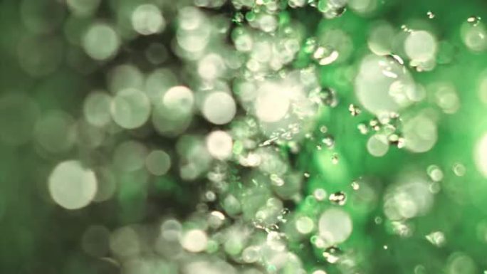 绿色霓虹灯照亮的飞溅水的超慢动作。振动下降分离并反弹成单独的元素。表面张力。
