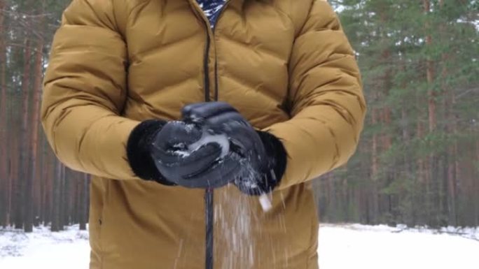 一个穿着黄色羽绒服和黑色手套的男人在他的手上扔了一个雪球。