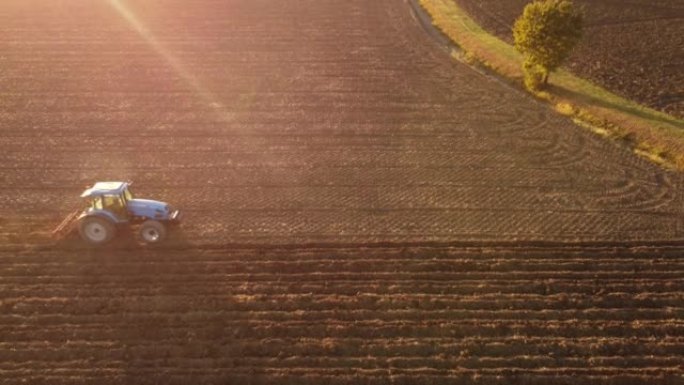 4k无人机镜头农民在日落时驾驶拖拉机深耕土地