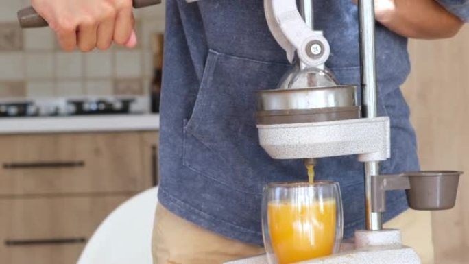 青少年在厨房做新鲜橙汁。男孩用特殊的厨房压榨装置挤压柑橘汁。