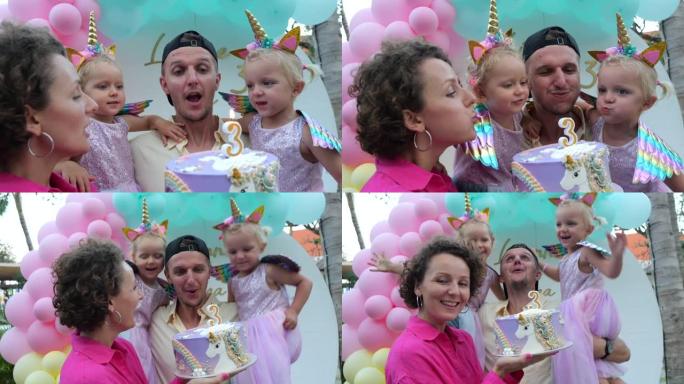 漂亮的孩子和父母一起庆祝他们的三岁生日。妈妈、爸爸和女儿们正在倒计时，吹灭蛋糕上的蜡烛，许愿。家庭度