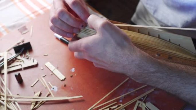人的手用胶水粘合船模胶合板细节，用手指握住。建造玩具船的过程，爱好，手工艺。工作台有各种材料、零件和