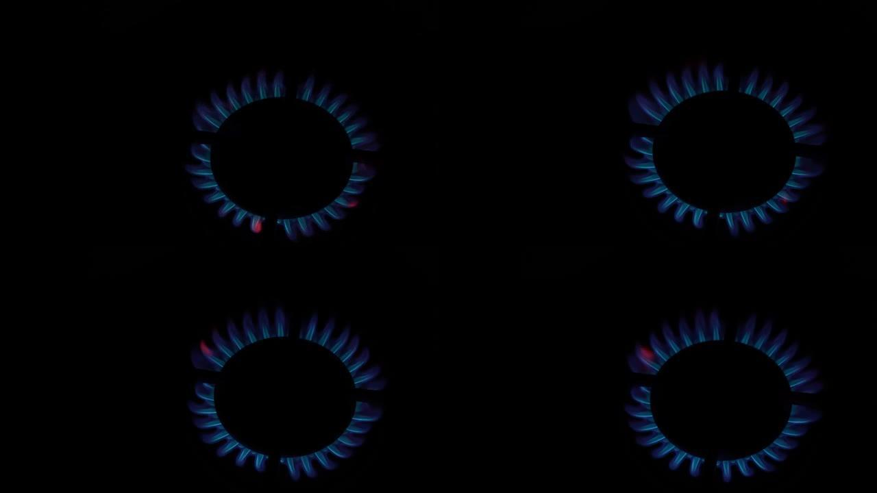 厨房炉灶上的煤气炉亮了。在黑色背景的黑暗中燃烧着蓝色的火焰。天然气发炎。天然能源载体，化石燃料