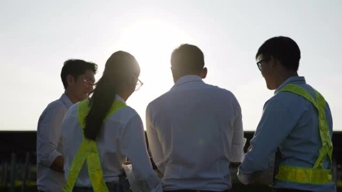 背光镜头，亚洲工程团队后视组在计划操作和站内光伏太阳能电池板使用笔记本电脑，年轻检查员工程师男女计划