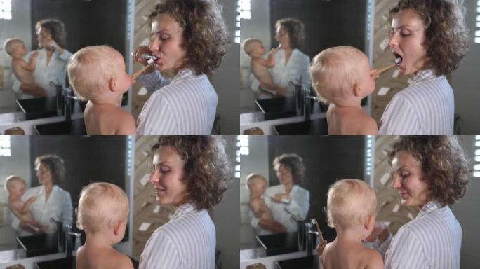 年轻的高加索母亲抱着婴儿一起刷牙。他们每天都有自己的晨练。他们一起刷牙很开心。