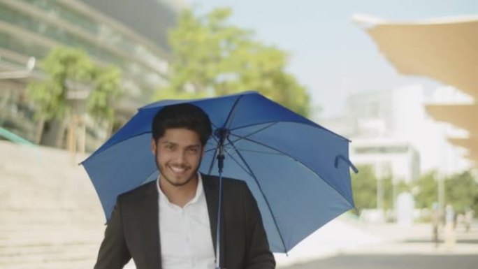年轻的穆斯林男子打开蓝伞，躲避阳光。