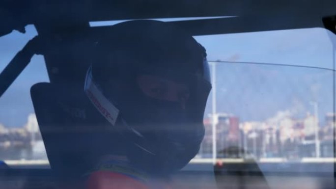 戴着黑色头盔的驾驶员坐在汽车上，表情满意