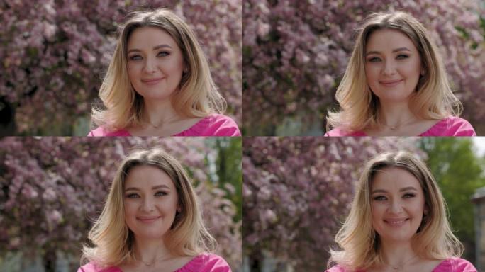 美丽的乌克兰女人的肖像。女孩站在樱花树前与鲜花和微笑。春天晴朗的一天。近距离视图