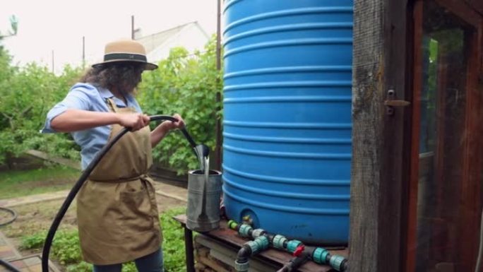 戴着草帽的特写女园丁从桶到喷壶收集水，为花园和果园浇水