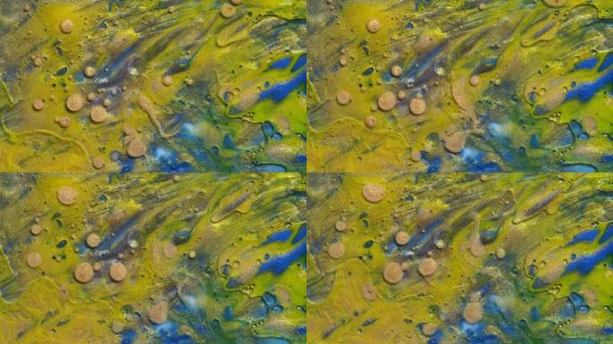 彩色金色和黄色丙烯酸涂料，气泡散布在蓝色表面上，以抽象的设计和纹理混合。闪闪发光的金色颗粒，墨球滴和