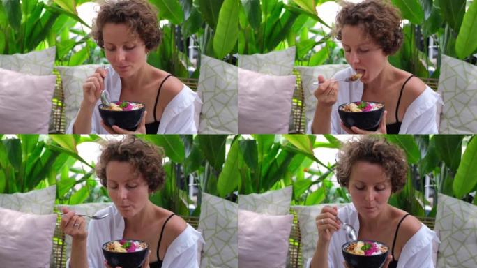 卷毛女孩坐在酒店的陶瓷碗中品尝热带水果早餐，享受异国健康饮食。女人喜欢吃糖和脂肪含量降低的美味甜点。