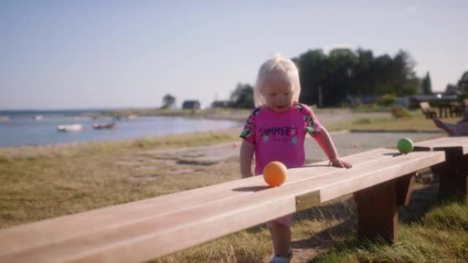 小女孩在木凳上玩滚滚的橙色球
